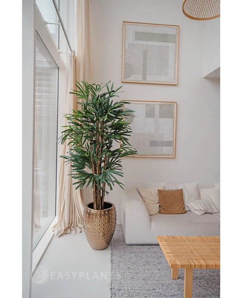 In einem hellen, modernen Wohnzimmer mit weißem Sofa, beigen Kissen, geflochtenem Tisch und abstrakter Kunst steht eine 180 cm große künstliche Palme in der Nähe eines großen Fensters. Mit seinen neutralen Farbtönen und dem Charme grüner Kunstpflanzen sorgt es für einen gemütlichen, minimalistischen Stil.