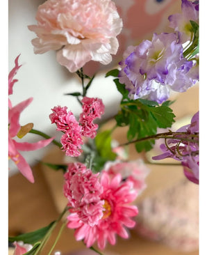 Eine Nahaufnahme des künstlichen Zweigs Statice 64 cm rosa, mit zartrosa Statice-Blüten und grünen Blättern, arrangiert in einem Blumenstrauß vor einem sanft verblassten Innenhintergrund.