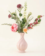 Der Kunstblumenstrauß Pretty Petite aus Seide in einer pastellrosa Vase enthält handgefertigte rosa und orangefarbene Blumen, weiße Blumen, grüne Blätter und rote Beeren – perfekt für eine nachhaltige Inneneinrichtung vor einem schlichten, hellen Hintergrund.