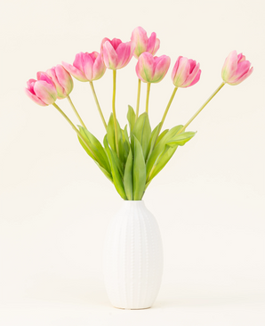 Der künstliche Seidenblumenstrauß French Tulip Pink ist in einer weißen Vase mit rosa französischen Tulpen und grünen Blättern vor einem einfachen hellen Hintergrund arrangiert.