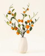 Der künstliche Blumenstrauß „Mandarin“ aus Seide besteht aus einer weißen, strukturierten Vase und Zweigen aus grünen Blättern und leuchtend orangefarbenen künstlichen Mandarinen, die vor einem schlichten, hellen Hintergrund eine lebendige Note verleihen.
