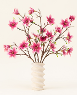 Der künstliche Blumenstrauß Magnolia Pink aus Seide ist in einer gewellten weißen Keramikvase mit grünen Knospen arrangiert und bildet eine elegante Präsentation vor einem hellen Hintergrund.