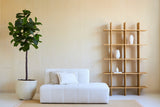 Minimalistisches Wohnzimmer mit einem weißen Sofa, zwei Kissen und einer Kunstpflanze Ficus Tabakpflanze Deluxe 180 cm neben einem offenen Holzregal mit weißen Vasen, alles vor einer beigen Wand und auf einem hellen Teppich.