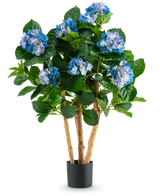 De Kunstplant Hortensia UV 85 cm blauw heeft hoge houten stelen en grote groene bladeren, met trossen blauwe en witte hortensiabloemen in een zwarte pot, perfect voor decoratie.