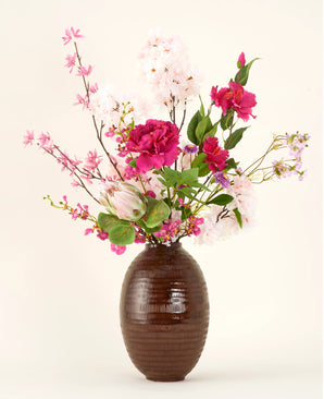 Der Kunstblumenstrauß Pink Reverie aus Seide befindet sich in einer Vase mit brauner Struktur, mit rosa, magentafarbenen und weißen Kunstblumen mit grünen Blättern vor einem schlichten hellen Hintergrund.