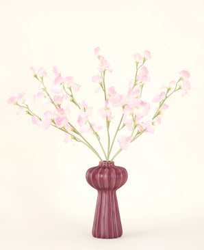 Der Seiden-Kunstblumenstrauß Erbse in Hellrosa mit mehreren hellrosa Erbsenstielen in einer gerippten burgunderfarbenen Vase steht vor einem hellen Hintergrund – ideal für jedes Kunstblumen-Interieur.