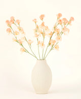 Die cremefarbene Keramikvase enthält den Kunstblumenstrauß Pea Peach aus Seide mit zarten pfirsichfarbenen und hellrosa Blüten mit langen grünen Stielen vor einem hellen, neutralen Hintergrund.