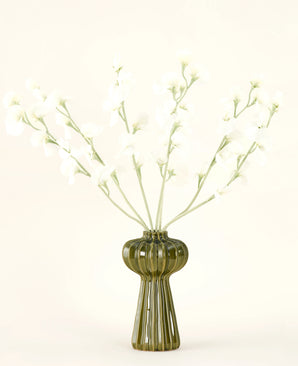 In einer grünen, gerippten Glasvase befindet sich der künstliche Seidenblumenstrauß Erbsencreme mit zarten weißen Seidenblumen und schlanken Stielen vor einem schlichten, cremefarbenen Hintergrund.