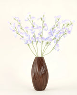 In einer braunen, gerippten Vase befindet sich der künstliche Seidenblumenstrauß Erbsen-Lavendel mit zarten Blütenblättern und grünen Stielen vor einem schlichten, cremefarbenen Hintergrund für eine dezente Landhausatmosphäre.