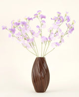 Eine strukturierte braune Vase hält den künstlichen Seidenblumenstrauß Erbsenlila-hellviolette Seidenblumen mit grünlichen Stielen vor einem schlichten, hellen Hintergrund.