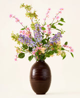 In einer dunkelbraunen Vase steht ein Strauß rosa, violetter und gelber künstlicher Seidenblumen, der „Sky Kiss“-Strauß, mit grünen Blättern, vor einem schlichten hellen Hintergrund. Diese wartungsfreie Dekoration sorgt für dauerhafte Schönheit in jedem Raum, ohne dass eine Wartung erforderlich ist.