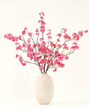 Der künstliche Blumenstrauß aus Seide, Kirschblüten-Fuchsia, 150 cm, besteht aus leuchtend fuchsiafarbenen Kirschblütenstielen mit grünen Blättern in einer schlichten weißen Vase, die vor einem hellen Hintergrund jedes Interieur ergänzt.