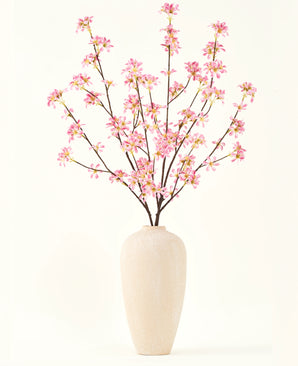 Eine hohe beige Keramikvase enthält mehrere Zweige des künstlichen Blumenstraußes aus Seide. Rosa Blumen mit zartrosa Blüten und grünen Blättern vor einem schlichten weißen Hintergrund.