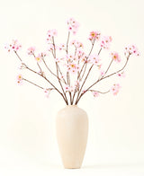Der Seiden-Kunstblumenstrauß Kirschblütenrosa 114 cm hat lange, dünne Zweige mit Büscheln hellrosa Blüten in einer beigen Keramikvase, die einen auffälligen Kontrast zum schlichten weißen Hintergrund bilden.