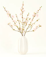 Der Seidenblumenstrauß Kirschblüten hellrosa 94 cm besteht aus zartrosa künstlichen Kirschblüten in einer weißen Keramikvase, die vor einem schlichten hellen Hintergrund Eleganz verleiht.