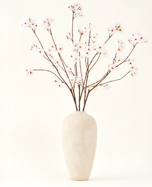 Der künstliche Seidenblumenstrauß Cherry Blossom Blush 114 cm hat hohe, zarte Zweige in einer schlichten beigen Vase, die Ihrem Interieur vor einem schlichten, hellen Hintergrund eine sanfte, elegante Note verleiht.