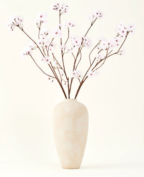 De Zijden kunstbloemen boeket Kersenbloesem lichtroze 114 cm staat in een hoge vaas van beige keramiek met lange, dunne takken en delicate lichtroze bloemen, waardoor een sereen kunstbloemen accent ontstaat tegen een effen achtergrond.