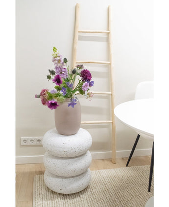 Eine künstliche Blumen-Glockenblume von 62 cm Lila steht in einer Vase auf drei runden, weißen, steinähnlichen Kissen. Dahinter steht eine helle Holzleiter vor einer weißen Wand, daneben ein weißer Tisch und Stuhl auf einem beigen Teppich.