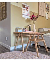 Eine moderne Wohnzimmerecke mit einem hellen Couchtisch aus Holz mit den künstlichen Anemonenzweigen 56 cm rosa in einer rosa Vase, zusammen mit einer Lampe und Büchern. Daneben steht eine beige Couch, akzentuiert durch Wandkunst und eine galerieartige Fototafel an der gelben Wand.