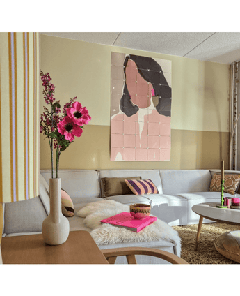 Ein gemütliches Wohnzimmer mit einem hellgrauen Sofa, rosa und goldenen Akzenten, einer künstlichen Anemone mit Zweigen von 56 cm in Rosa in einer modernen Vase, einem Couchtisch mit einem Pelzteppich und pastellfarbener abstrakter Kunst einer Frau an der Wand.