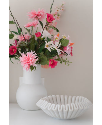 Eine weiße Vase mit einer künstlichen Blume Rhododendron Azalee 73 cm Fuchsia steht neben einer weißen Schale aus gerippter Keramik auf einer glatten Oberfläche vor einem neutralen Hintergrund.