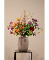 Der künstliche Hartriegel Real Touch Light Yellow 74 cm, eine lebensechte hellgelbe Kunstblume, steht in einer Keramikvase mit grünem Blattwerk auf einem schwarzen Metallständer vor einem schlichten beigen Hintergrund.