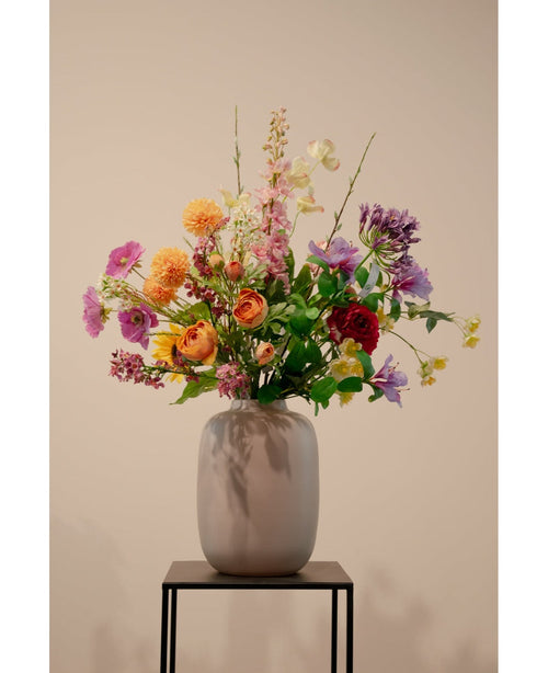 Der künstliche Hartriegel Real Touch Light Yellow 74 cm, eine lebensechte hellgelbe Kunstblume, steht in einer Keramikvase mit grünem Blattwerk auf einem schwarzen Metallständer vor einem schlichten beigen Hintergrund.