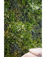 Eine üppige, strukturierte Kulisse wird durch die vertikale UV-Gartenwand Kunsthaag Freshness 100 x 100 cm geschaffen, die dicht mit grünem Blattwerk bedeckt ist. Unten rechts sind zwei gefaltete beige Handtücher zu sehen.