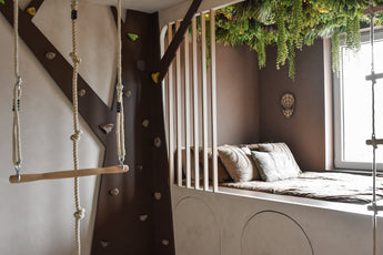 Ein gemütliches Kinderzimmer mit eingebautem Bett und Kissen wird mit der künstlichen Hecke Lush Deco Deluxe 100x100 cm UV dekoriert, die für üppiges Grün sorgt. Eine Kletterwand, Strickleiter und Schaukel sorgen bei Tageslicht für Baumhaus-Feeling.