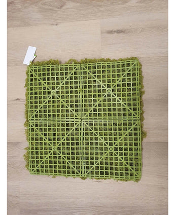 Das künstliche Haag Nordic Moss 50x50 cm UV ist eine grüne Kunstrasenmatte mit einer sichtbaren Kunststoffgitterrückseite, ideal für luxuriöse Innenräume oder die Schaffung einer grünen Wand. Es steht auf einem hellen Holzboden mit einem kleinen weißen Etikett in einer Ecke.
