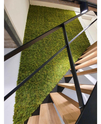 Eine moderne Treppe mit Holzstufen und schwarzem Geländer steht neben einer grünen Wand aus Kunsthaag Nordic Mos 50x50 cm UV und setzt einen natürlichen, strukturierten Akzent in der luxuriösen Inneneinrichtung.