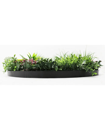 Die künstliche Hecke auf schwarzem Rahmen Ø100 cm ist ein schwarzer, halbrunder Blumentopf, gefüllt mit üppigem grünem Laub und einigen rosafarbenen Blättern, vor einem weißen Hintergrund.