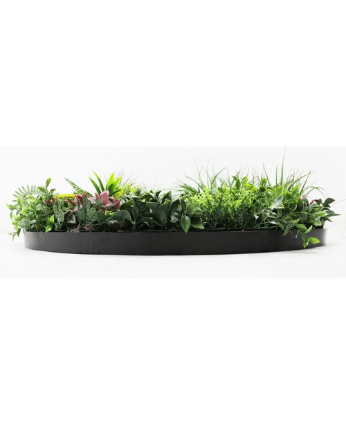 Die künstliche Hecke auf schwarzem Rahmen Ø100 cm ist ein schwarzer, halbrunder Blumentopf, gefüllt mit üppigem grünem Laub und einigen rosafarbenen Blättern, vor einem weißen Hintergrund.