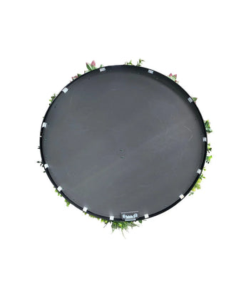 Eine künstliche Hecke auf einem Trampolin mit schwarzem Rahmen, Ø 100 cm, von oben gesehen mit grünen Blättern und rosa Blüten am Rand, vor einem weißen Hintergrund.