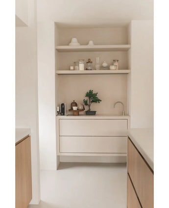 Minimalistische Küchenecke mit hellen Holzregalen mit Töpfen, Vasen, Dekor, einer Arbeitsplatte mit Kleingeräten und der 40 cm großen Topfpflanze „Artificial Bonsai Wacholder“, dazu eingebaute Schubladen und ein kleiner Wasserhahn – alles in neutralen Tönen.