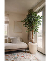 Ein modernes Wohnzimmer mit einem beigen Sofa, einem Kissen mit Streifen, abstrakter Wandkunst, einem gemusterten Teppich, einem raumhohen Fenster mit transparenten Vorhängen, die natürliches Licht hereinlassen, und einer Kunstpflanze Ficus Green 210 cm.